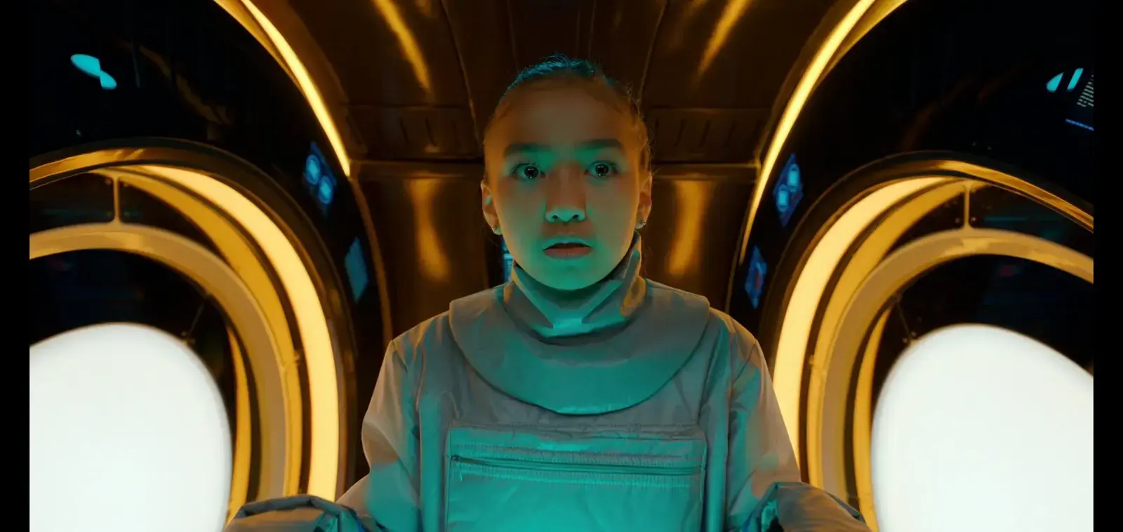 A woman in a space suit with a high-tech setting, surrounded by glowing circular structures, looks surprised or concerned.