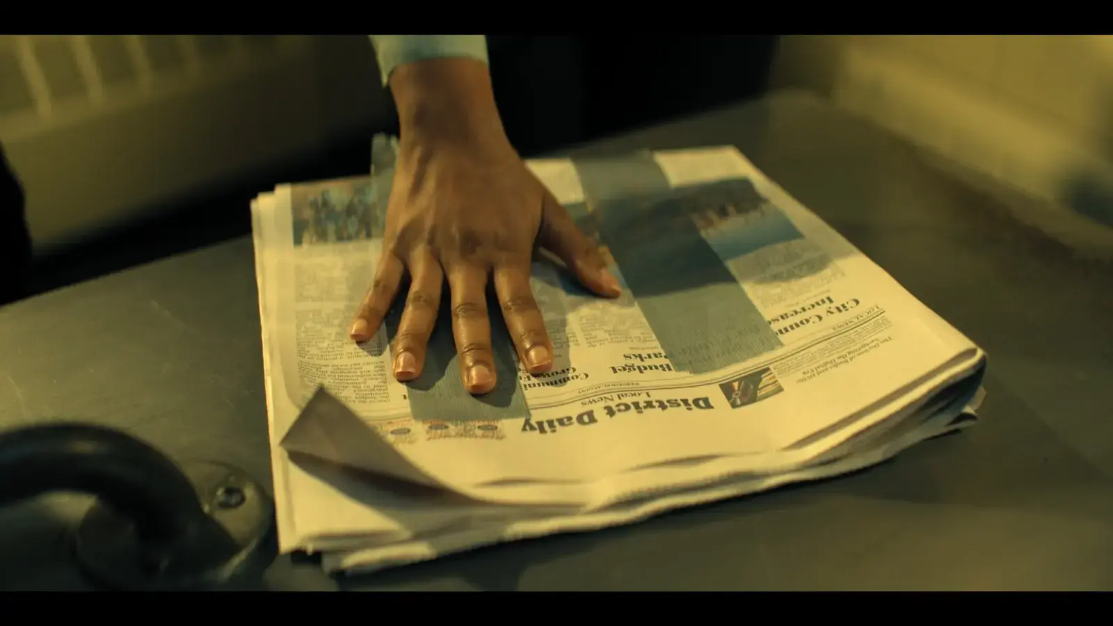 A person's hand pressing down on a folded newspaper on a table.