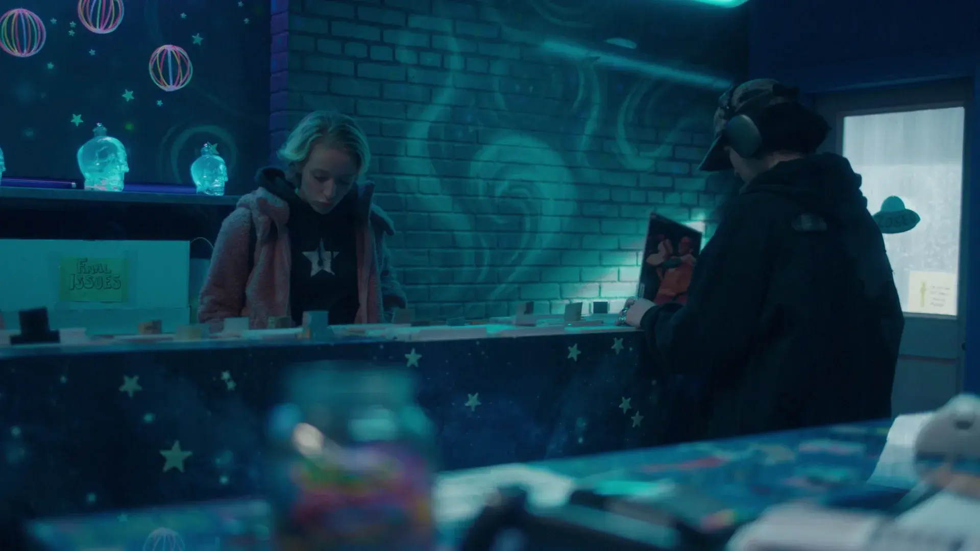 Customers at the comic shop counter, painted with stars and planets, under blue light