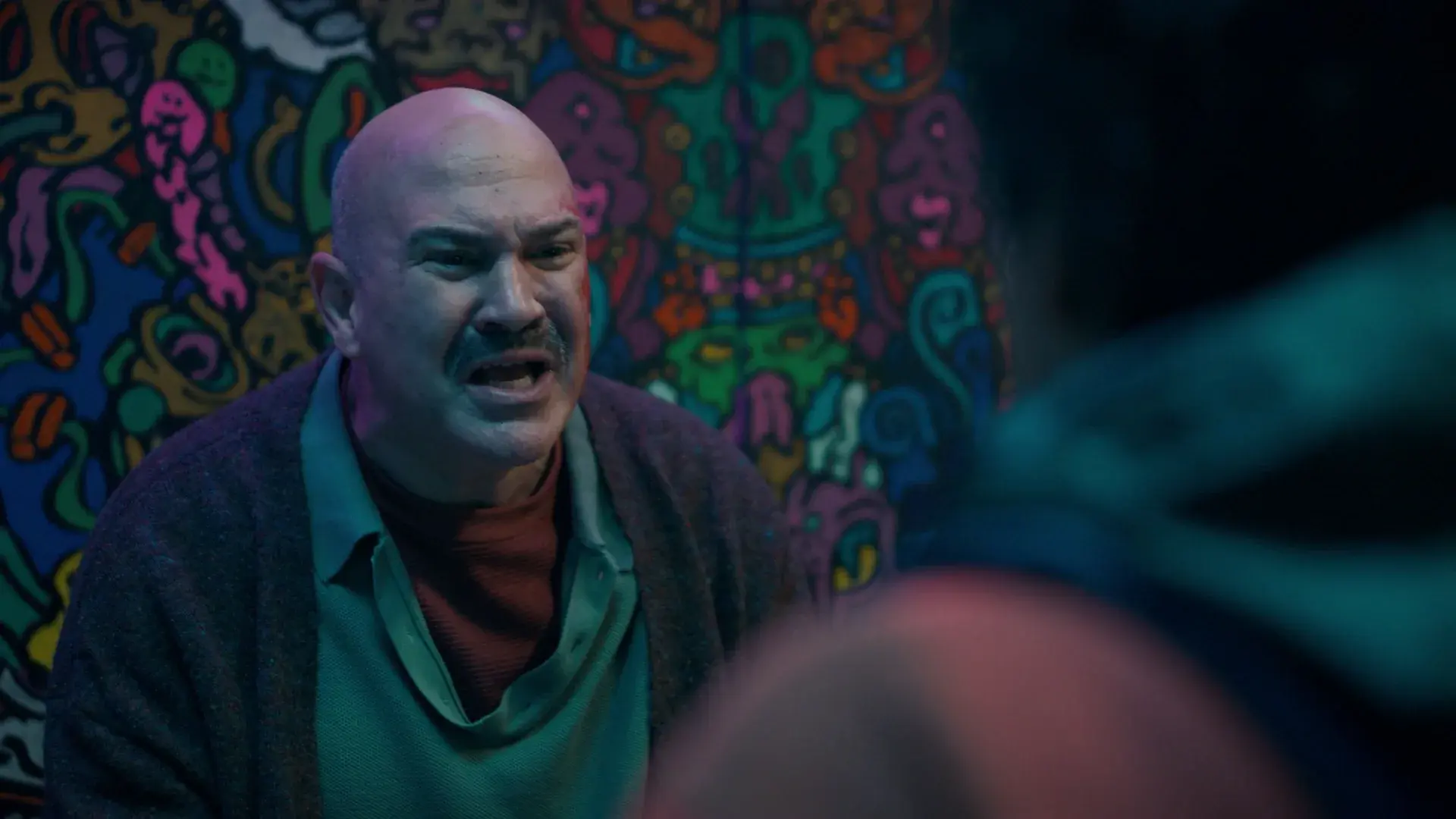The shop owner shouts in front of a wall of colourful psychedelic artwork