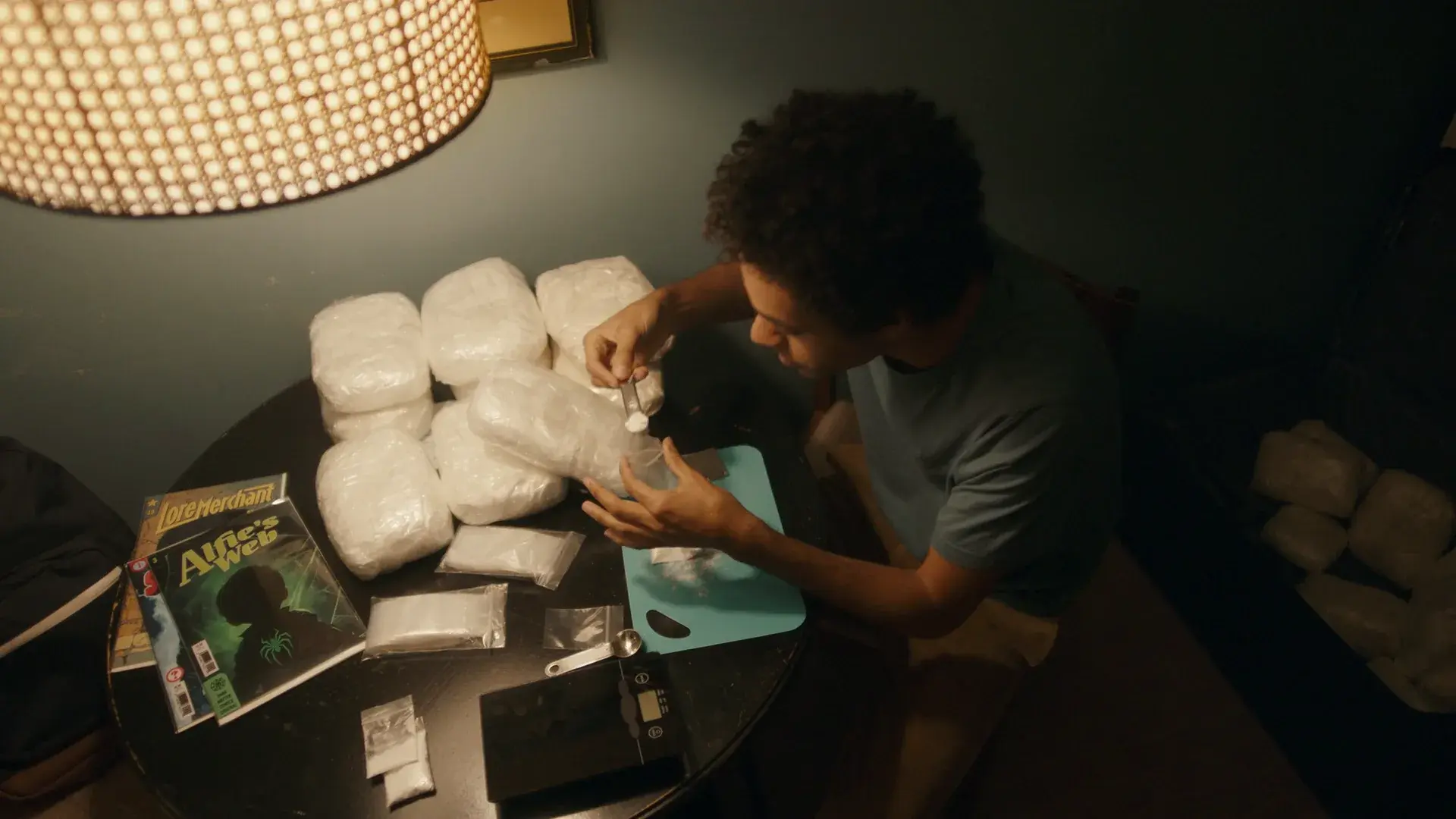 A young man at a table stacked with wrapped packages, beside a comic book