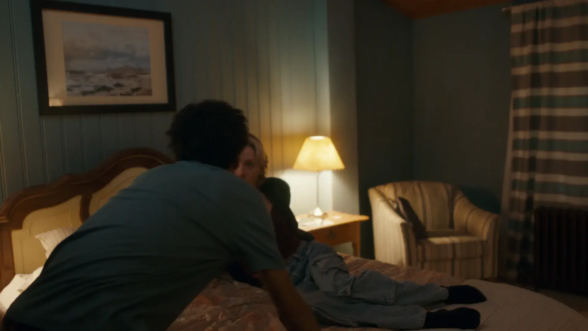 A dim motel room with a framed seascape print above the bed