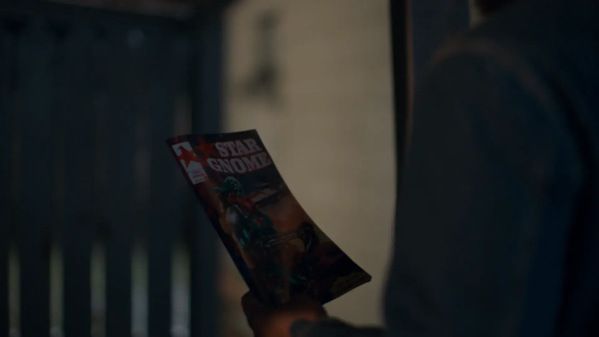 A hand holds up a Star Gnome comic book in a dark doorway