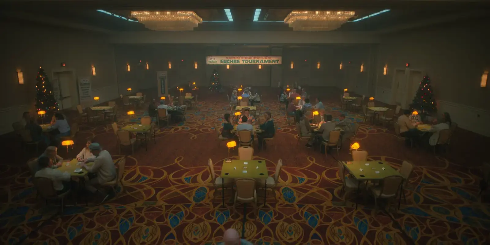 People playing poker at tables in a decorated banquet hall with Christmas trees, a banner for Eucre Tournament, and warm lighting.