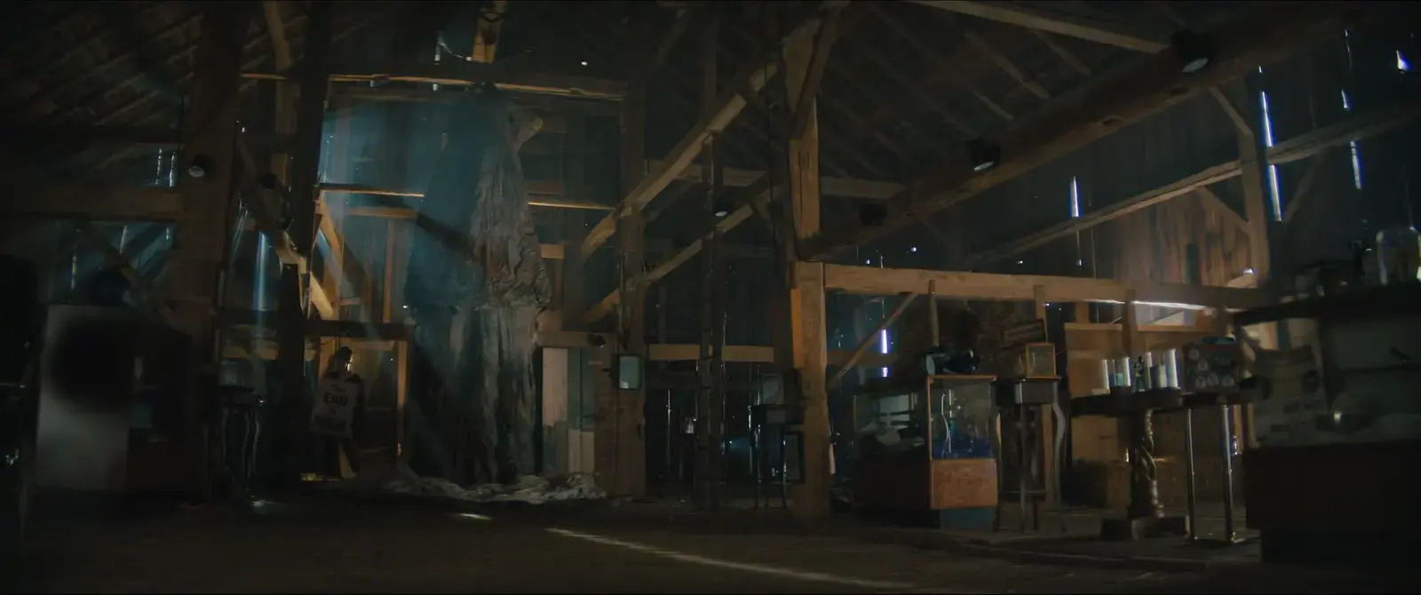 Interior of a rustic barn with wooden beams, shelves with various items, and sunlight streaming through gaps in the walls, creating beams of light.