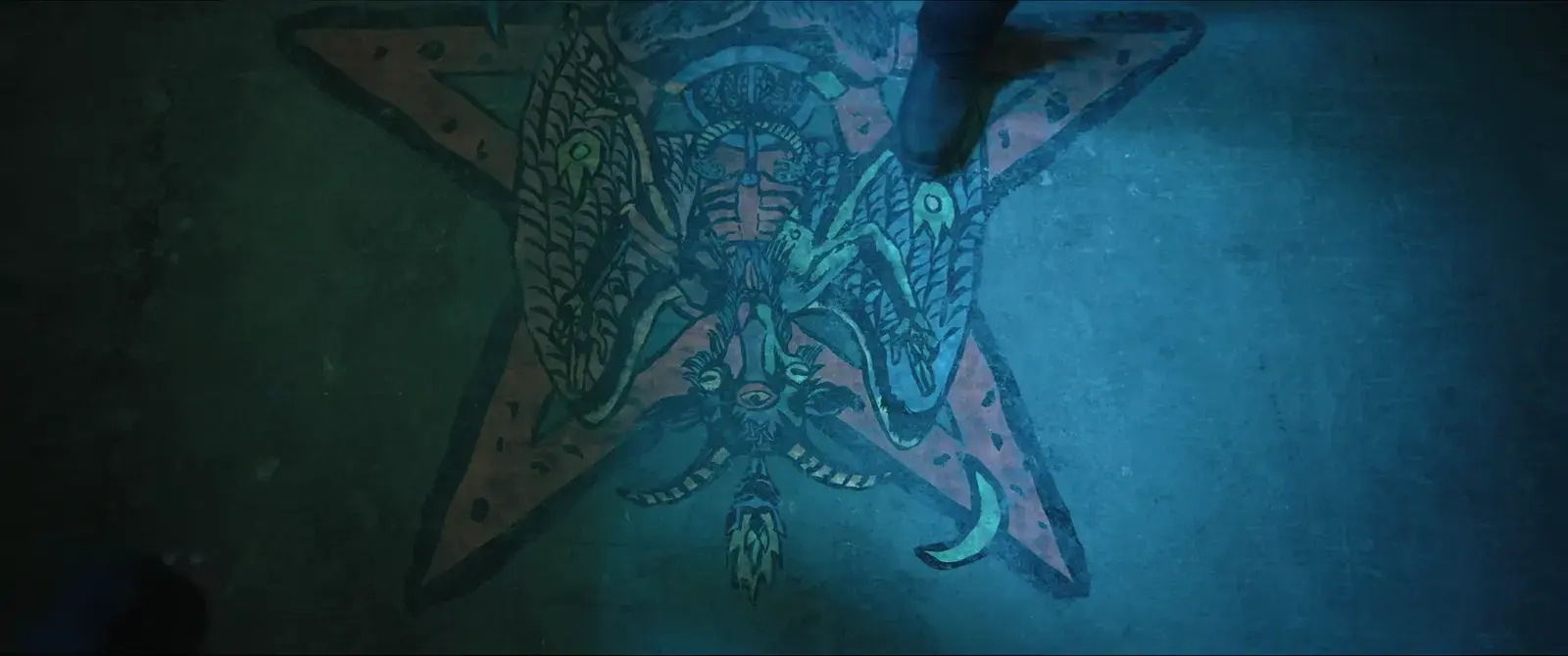 A person standing on a colorful star on the ground with a detailed design of a spiritual humanoid figure with the body of a crab and a face of a human, painted on the surface.