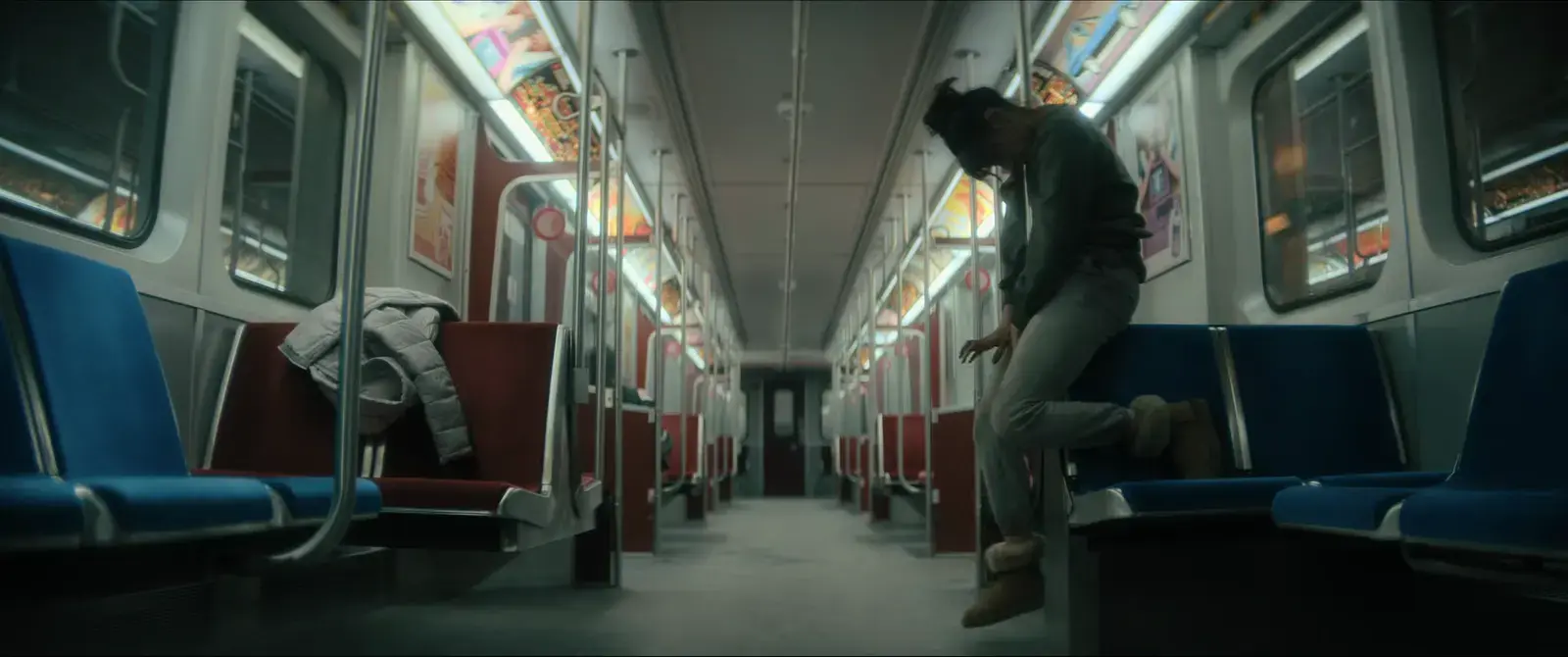 A woman sitting on a train seat with her head bowed and hands extended downward, empty train interior with blue and red seats, no other passengers.