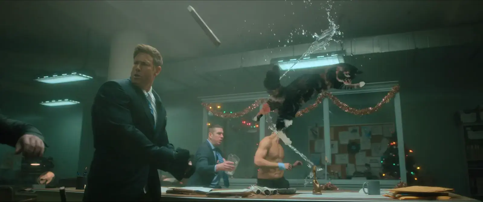 A chaotic scene in an office with a man in a suit looking shocked as a dog leaps off a table, spraying water from a hose.