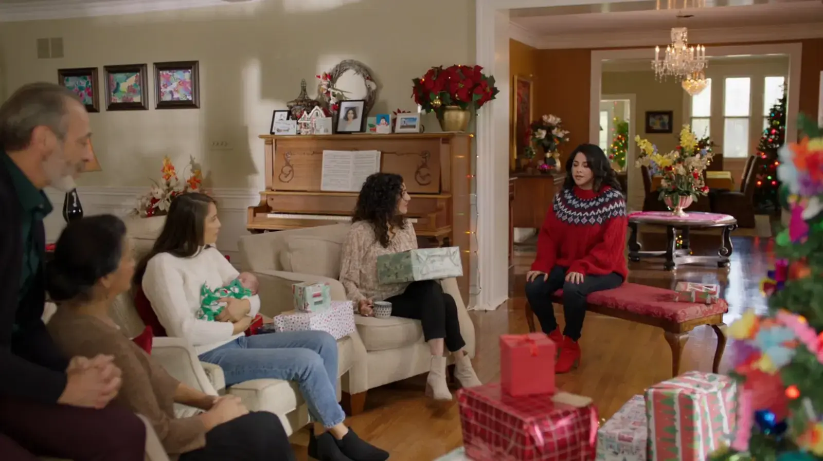 Family gathered in living room decorated for Christmas, with wrapped presents, a Christmas tree, and holiday decorations.