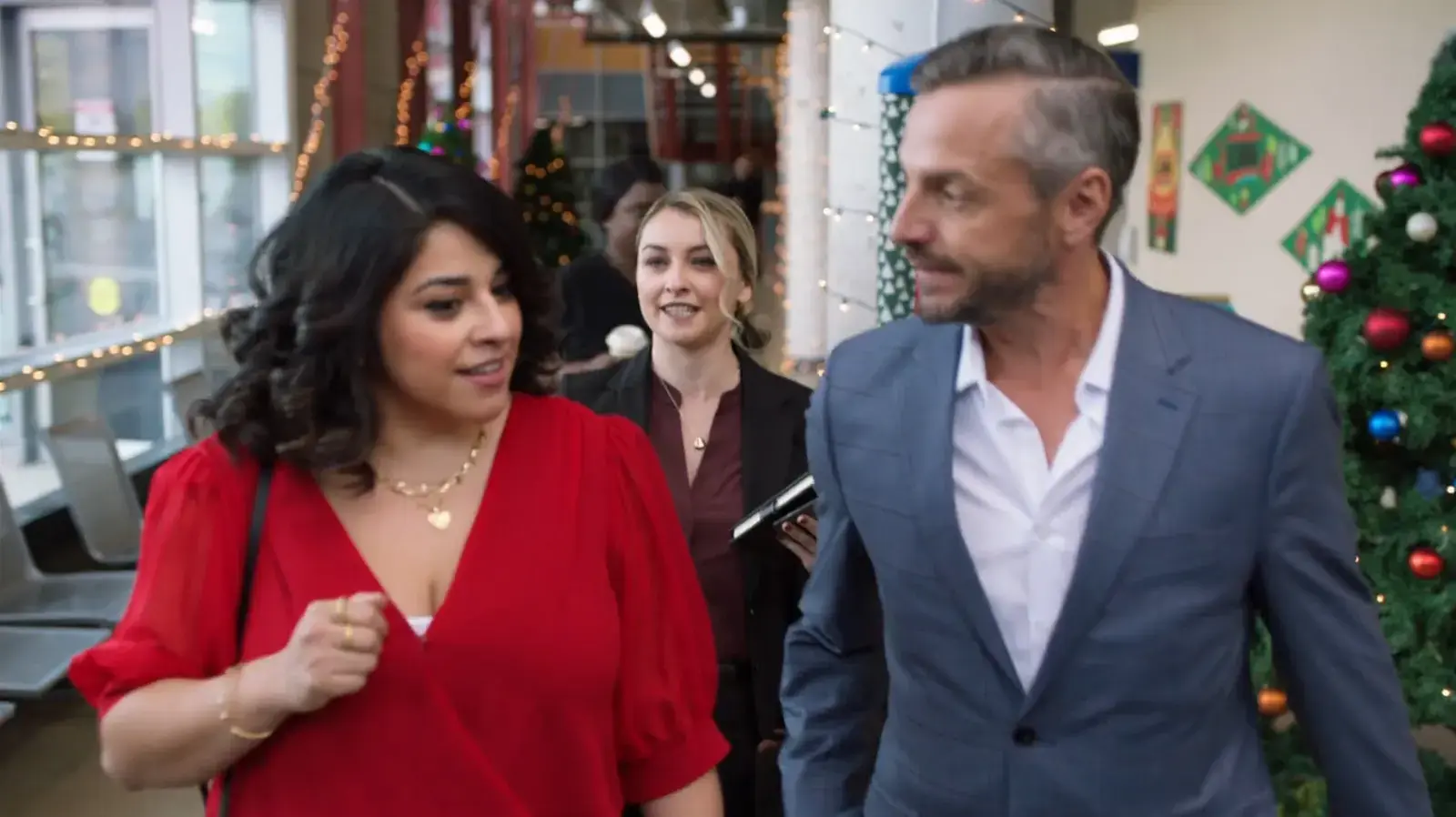 People talking at a holiday party with Christmas decorations, including a Christmas tree, in the background.